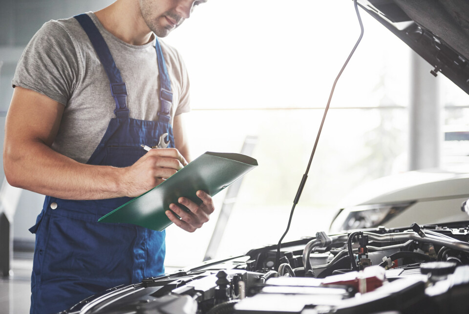 A mechanic holding a clipboard looks at a car with its bonnet up