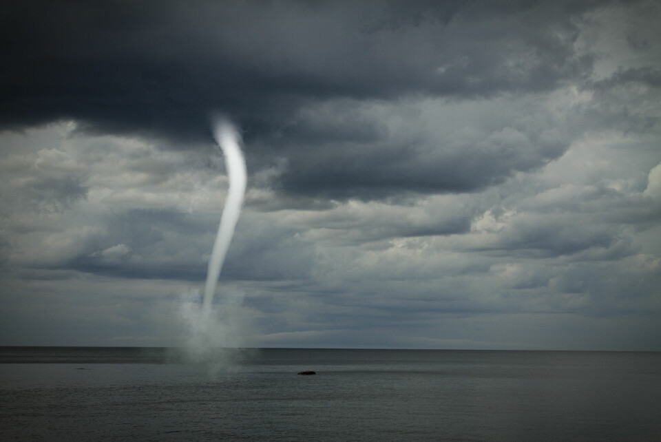 A photo of a small ‘waterspout tornado’ in a stormy sky off a coast
