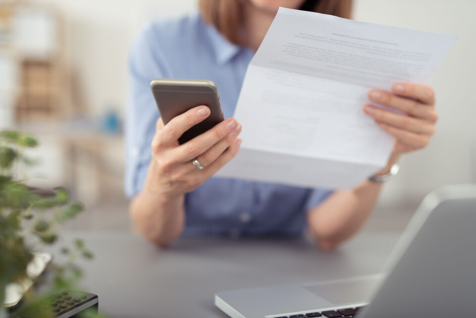 stockfour / Shutterstock A woman looking at a mobile phone and a piece of paper