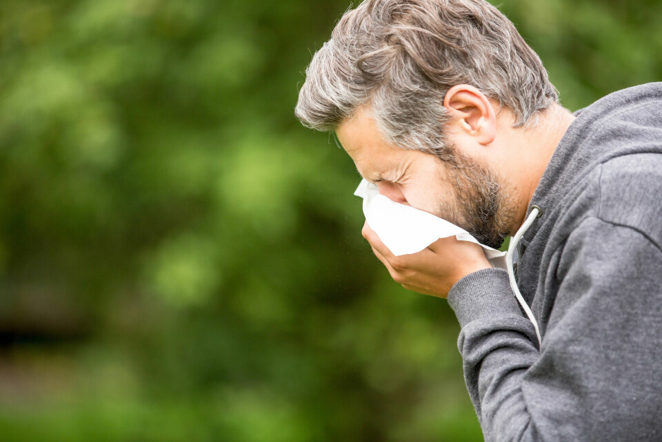 A man sneezes into a tissue against an outdoor background