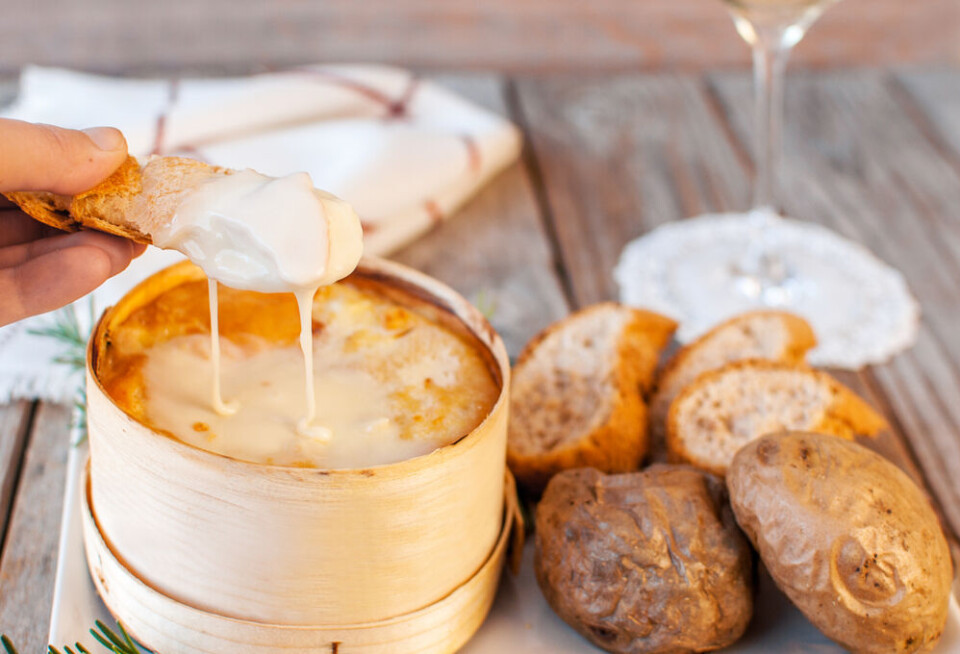 A view of someone dipping bread into a creamy Mont d’Or cheese box