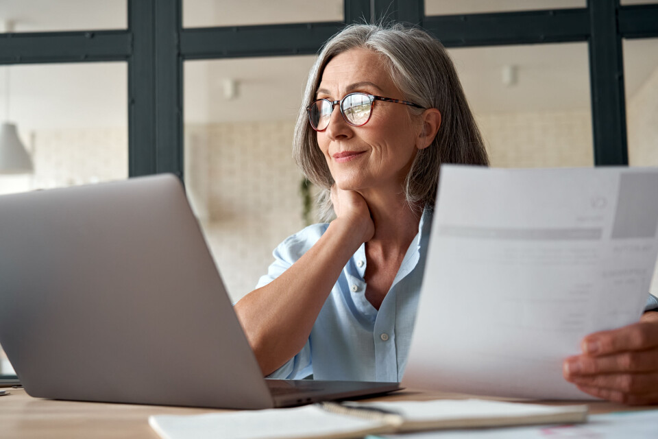 A woman holding a piece of paper and using a laptop