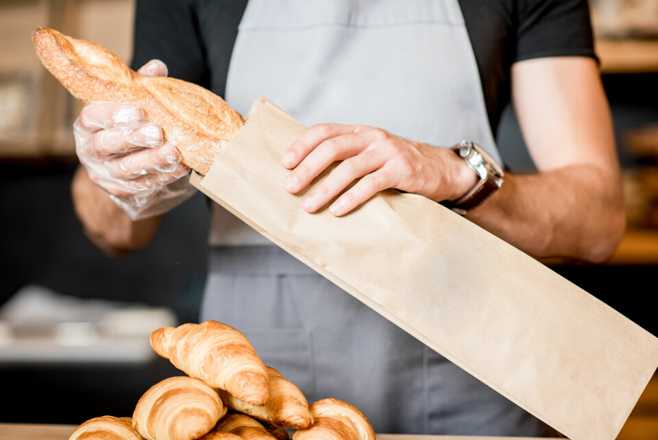 A baker puts a baguette in a paper bag
