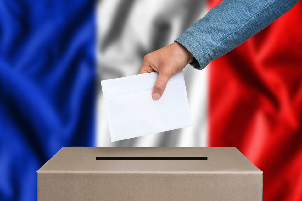 An image of a male hand dropping a ballot paper into the ballot box with a French flag in the background