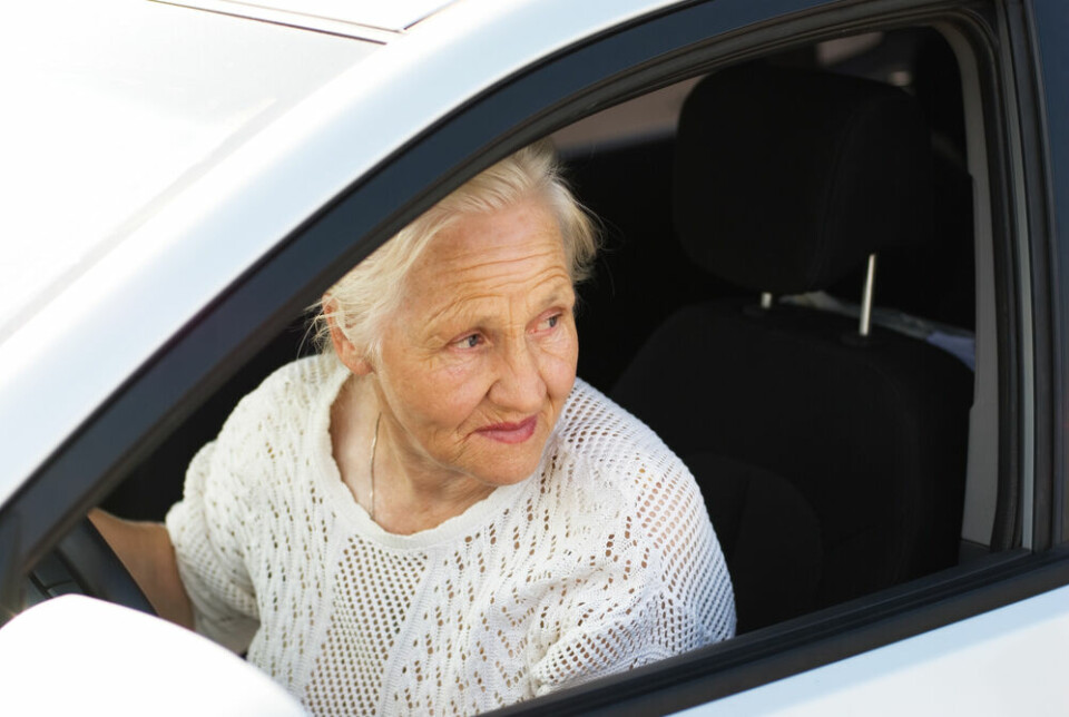 An older woman looking at the window of the car she is driving