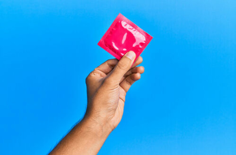 A photo of a man’s hand holding up a condom packet on a blue background