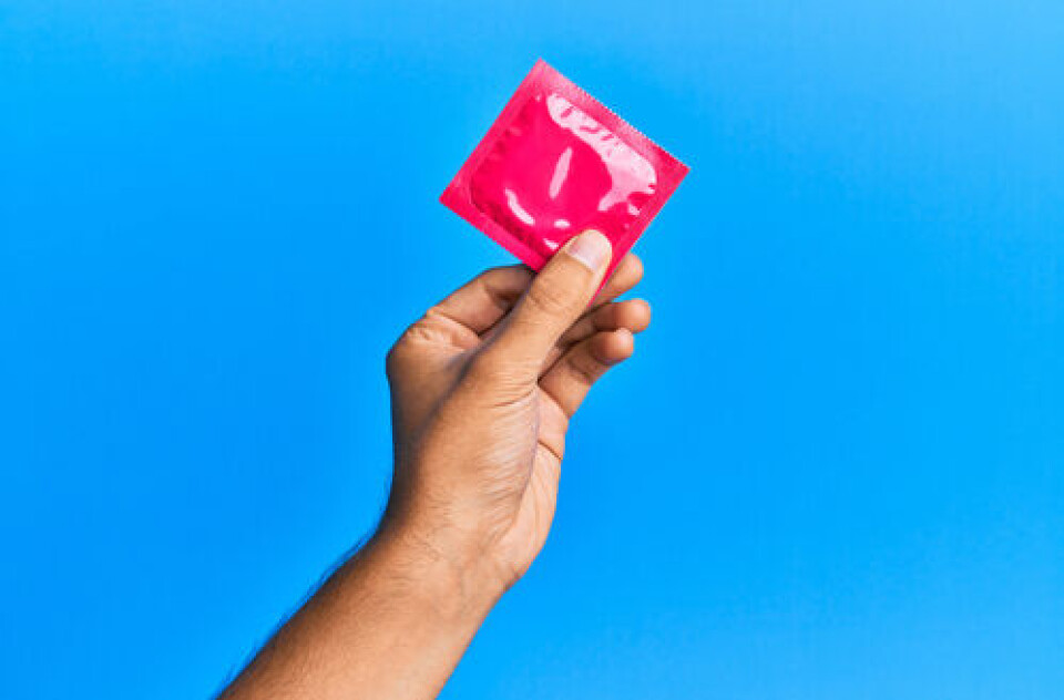 A photo of a man’s hand holding up a condom packet on a blue background