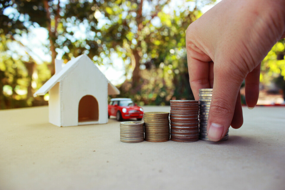 A concept of home and car insurance with models in the background and a hand lining up coins in the foreground