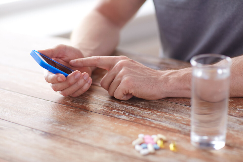 A man uses a smartphone next to a pile of tablets and a glass of water