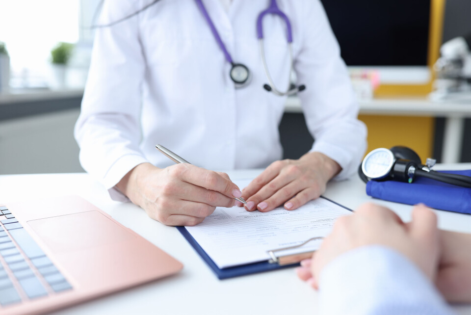 A photo of a GP writing on a clipboard while seeing a patient