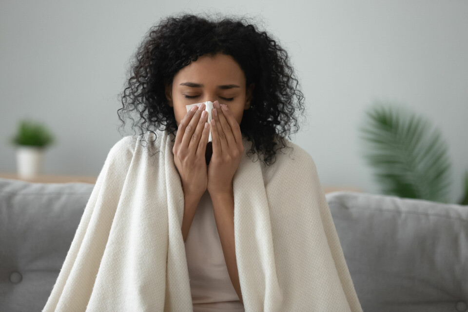 A woman sneezing, covered in a blanket