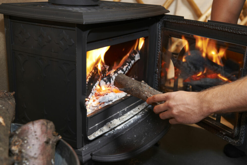 A photo of a man putting a log on a woodburning stove fire