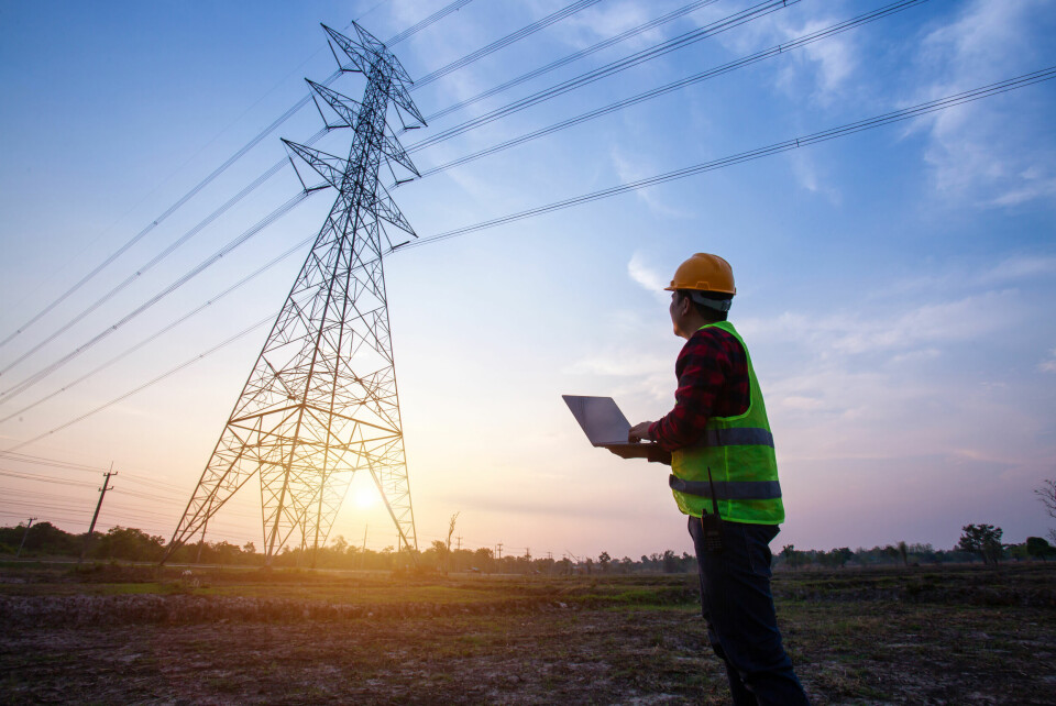 A photo of an engineer in a high-vis vest looking up at an electricity pylon