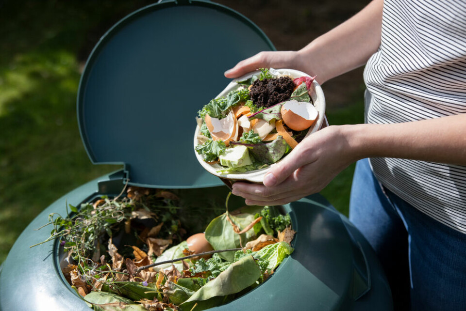 A woman emptying food leftovers into a compost bin in a garden