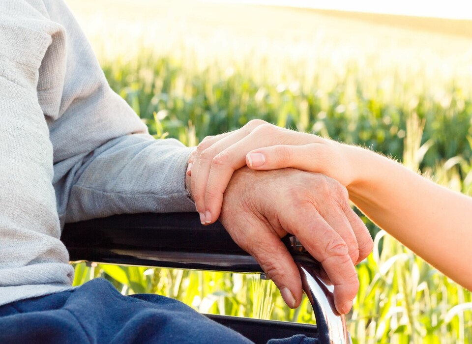 A man in a wheelchair with a carer’s hand on his arm