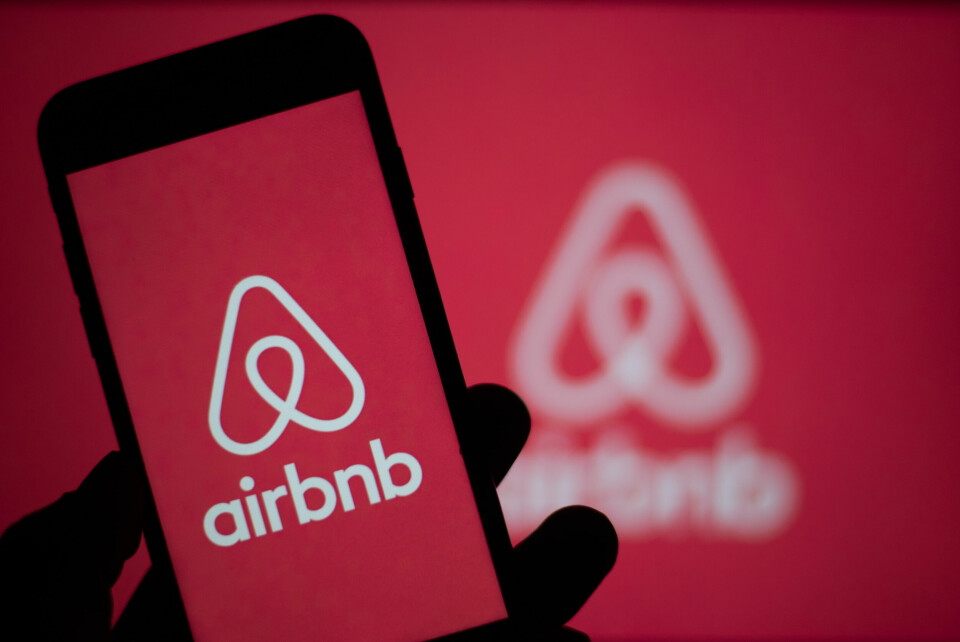 A photo of a smartphone showing the Airbnb logo with the same logo in the background