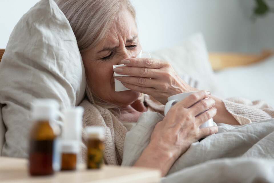 A photo of an older woman in bed with flu, with medicine and tissues