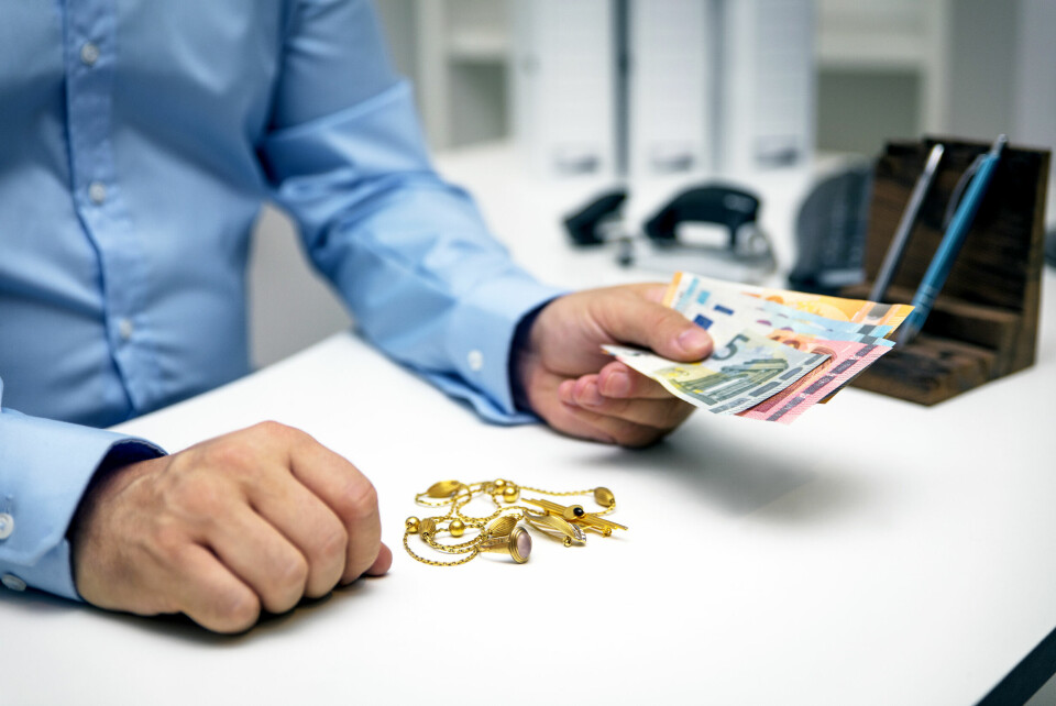 A man handing over cash with gold jewellery on a table