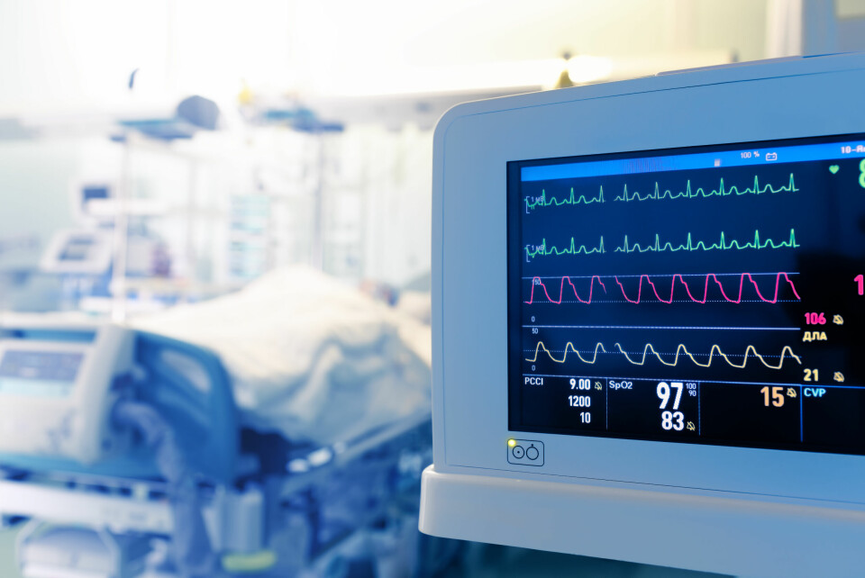 A screen showing the vitals of a patient in a bed behind in hospital intensive care