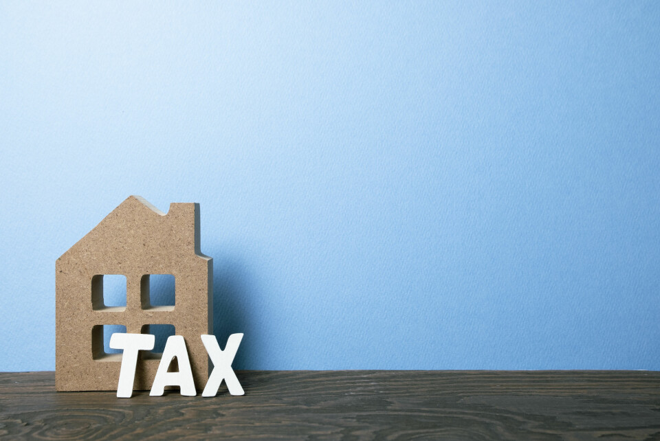 A photo of a model house with the words TAX in front of it, against a blue background