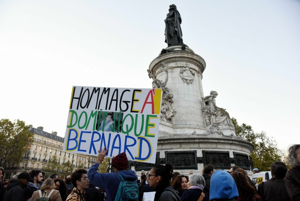 A view of a crowd of people gathered in support, with a banner reading: Homage to Dominique Bernard