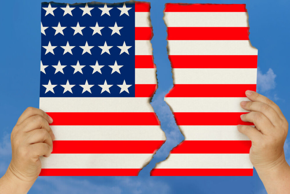 Hands holding a torn U.S. flag up against a sky blue background