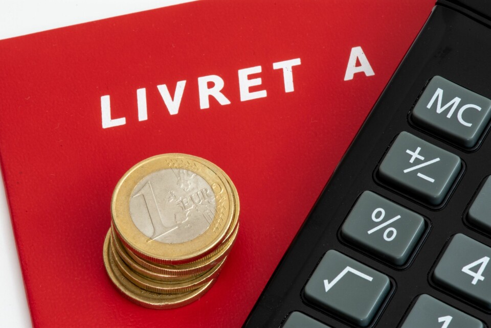 A Livret A red booklet with 1 euro coins piled on top of it, next to a calculator