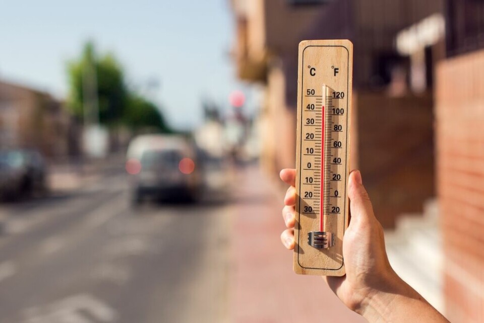 A man holding a thermometer showing 40C against an urban background