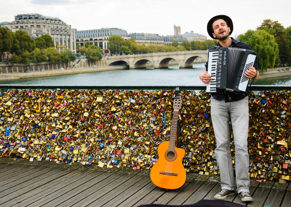 A young musician plays the accordion on the Love Locks Pont des Arts bridge next to a guitar