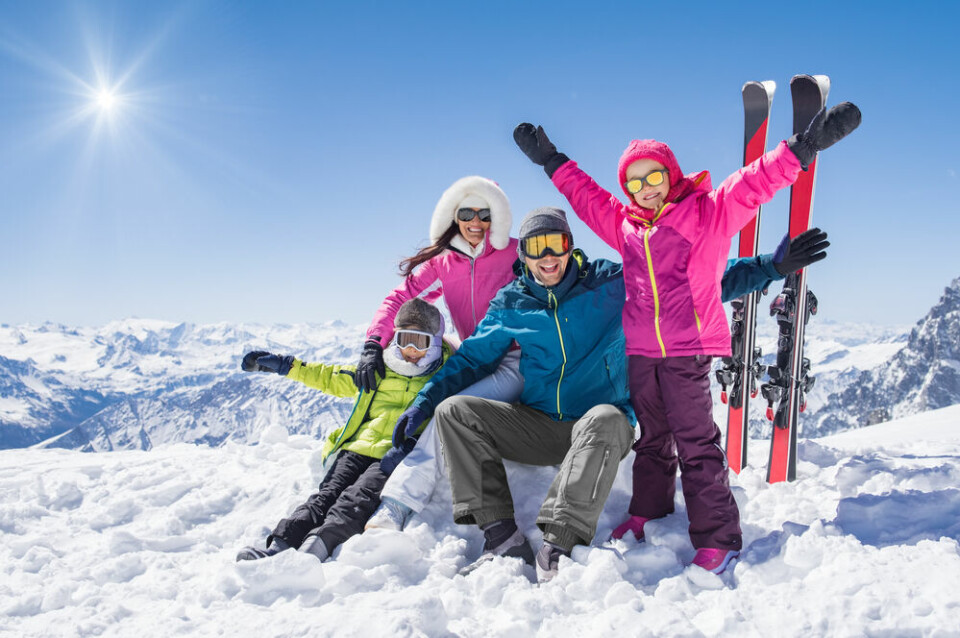 A family in ski suits on a mountain cheering at the camera