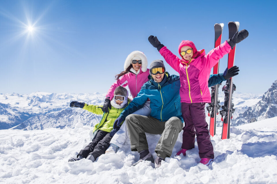 A family in ski suits on a mountain cheering at the camera