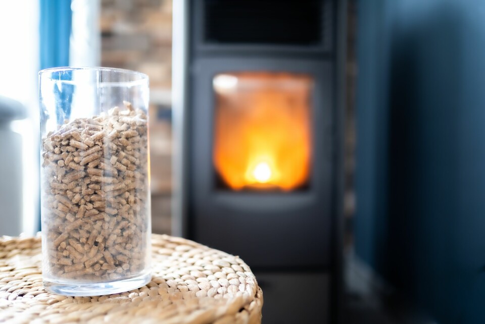 A photo of a wood pellet fuelled stove in the background with a glass of wood pellets in the foreground