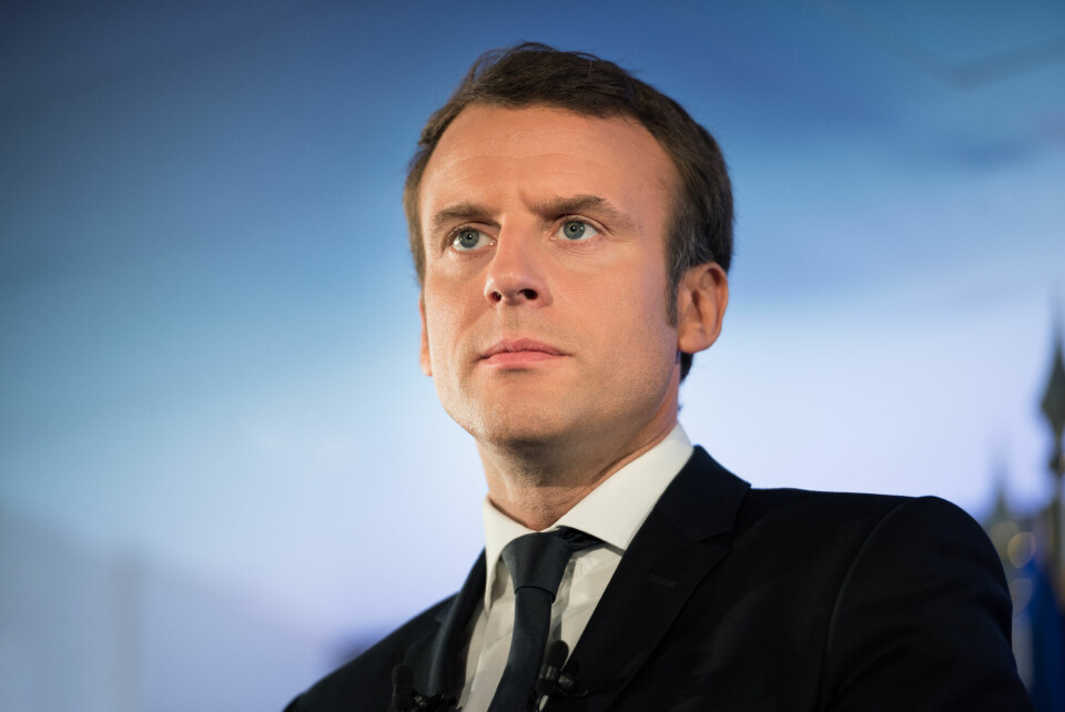 A photo of President Emmanuel Macron in a black suit, with a blue background