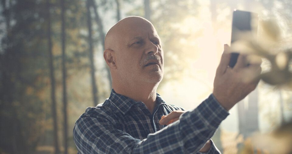 An older man looking annoyed at a phone, holding it up, outside