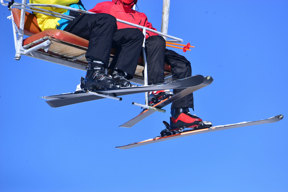 Two skiers sit on a mountain chair lift with their legs and skis dangling
