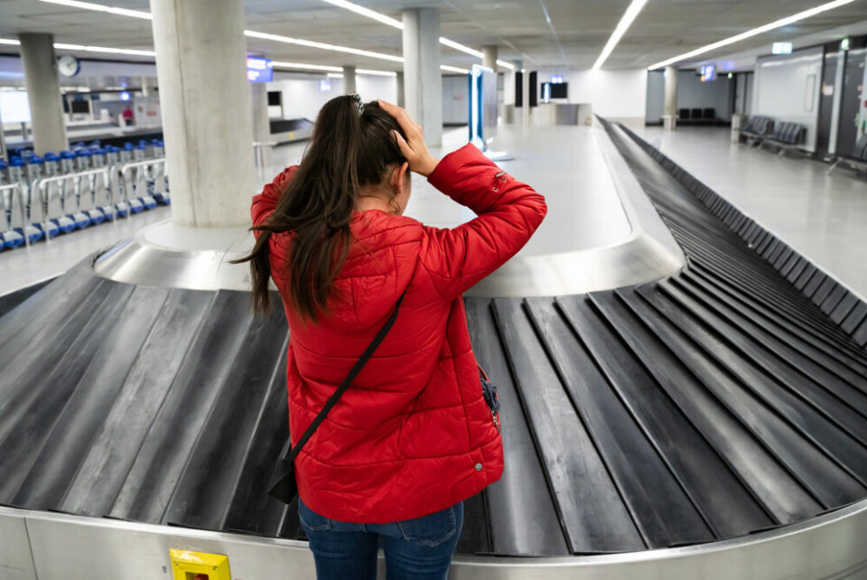 A woman in a red jacket holding her hands to her head next to an empty luggage conveyor belt at an airport