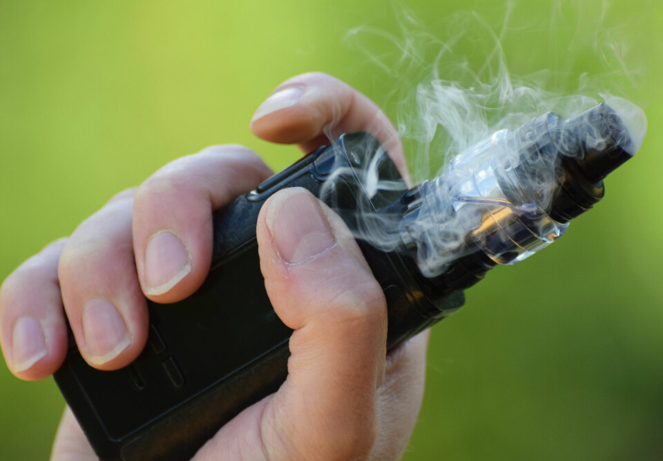A man vaping, his hand in close up holding an e-cigarette
