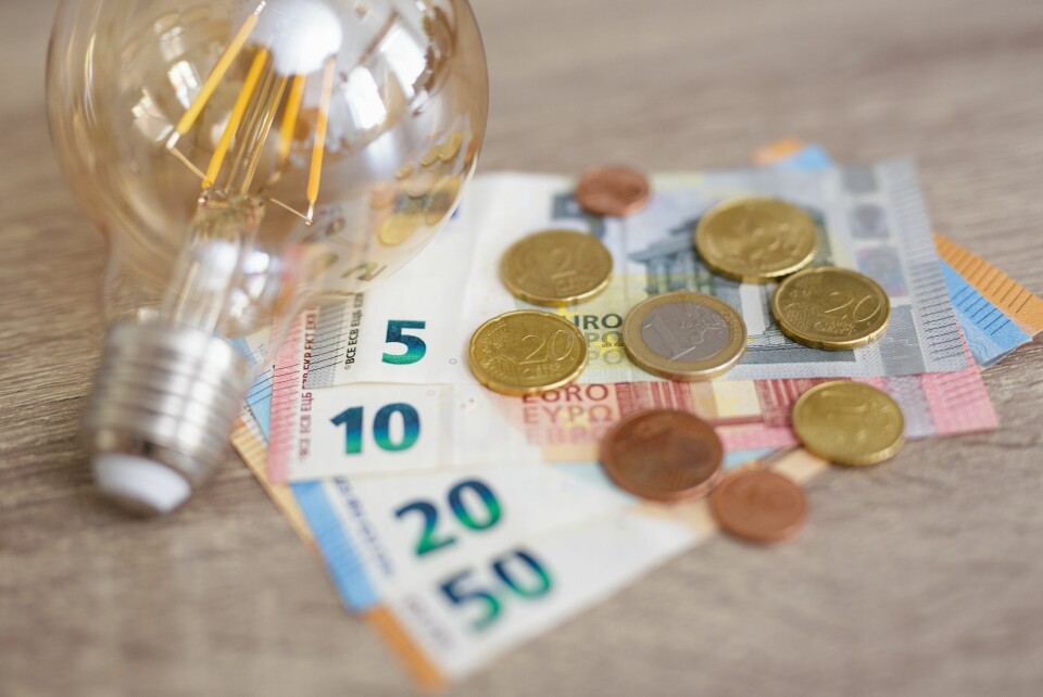 A lightbulb on a table with euro bills and coins, to show energy payment money