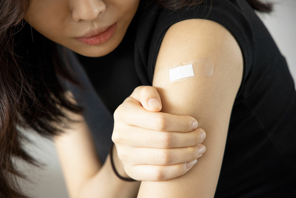 A woman looking at a plaster over a vaccination wound on her upper arm