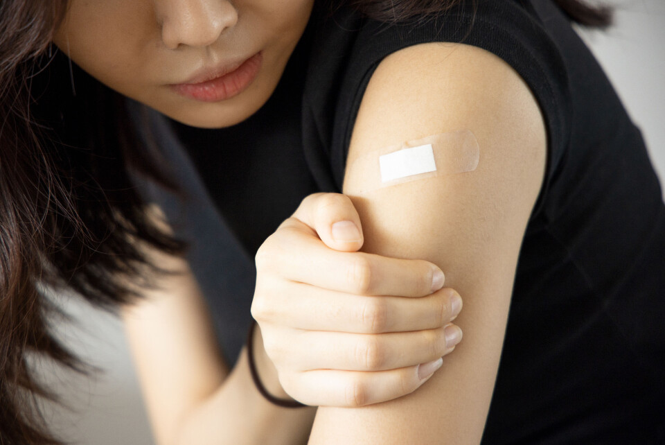 9nong / Shutterstock A woman looking at a plaster over a vaccination wound on her upper arm