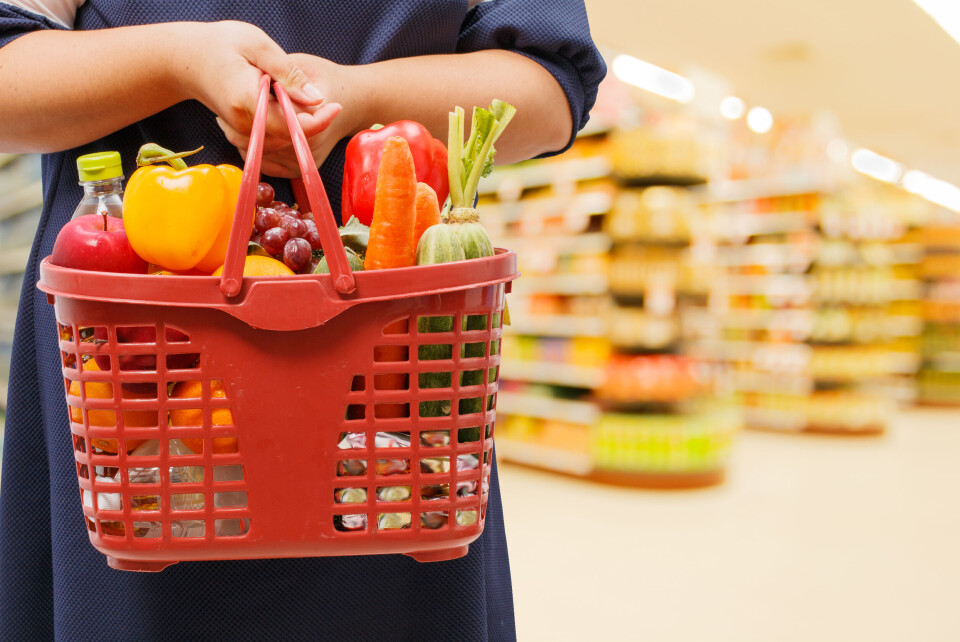 A woman holds a basket of fruit and veg in a supermarket