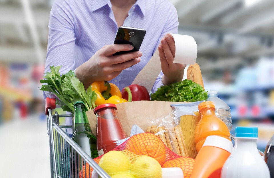 A photo of a woman with a shopping trolley holding a receipt, looking at her phone, to show rising prices