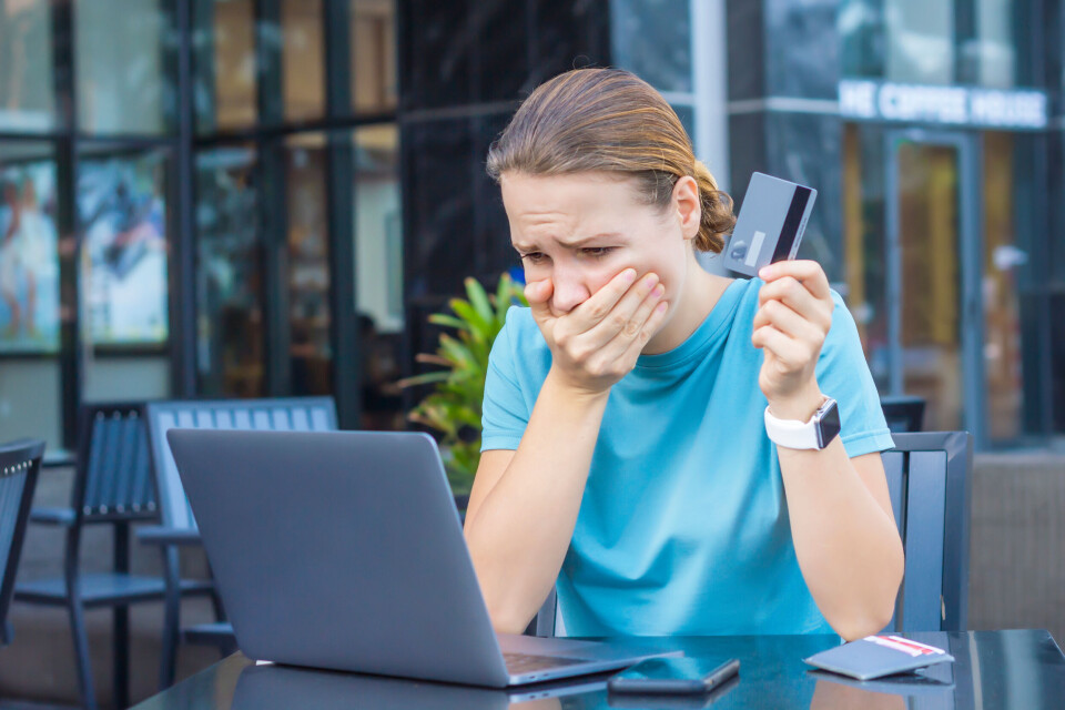 A woman holding a bank card, looking at her laptop with a shocked face