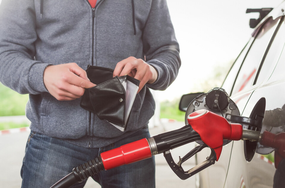 A man filling up his car with fuel looking into an empty wallet