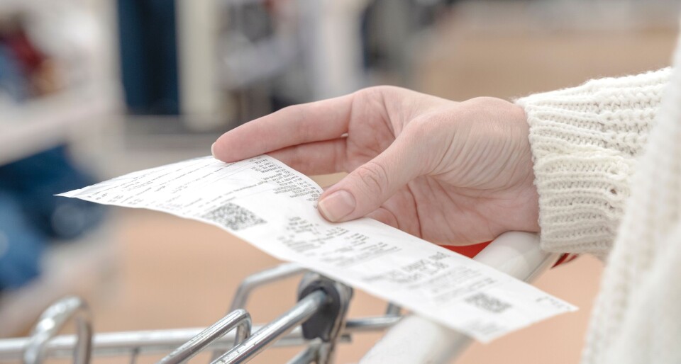 Ultraskrip / Shutterstock A person wearing a white jumper holding a receipt while pushing a trolley