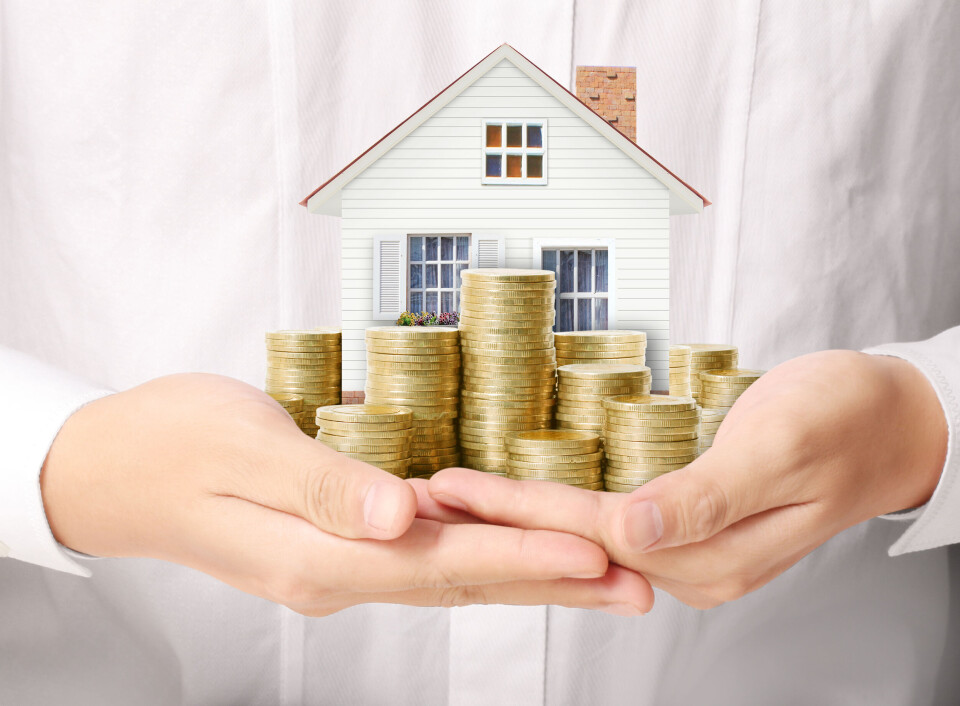 A photo of two hands holding a model house with coins, to show wealth and property assets