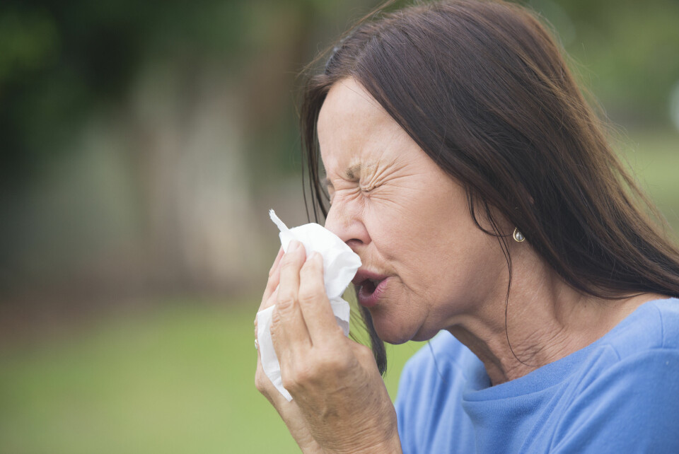 A woman sneezing into a tissue outdoors