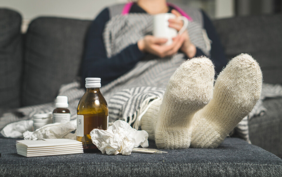 An image of a pile of tissues and a medicine bottle sitting at a sick person's feet