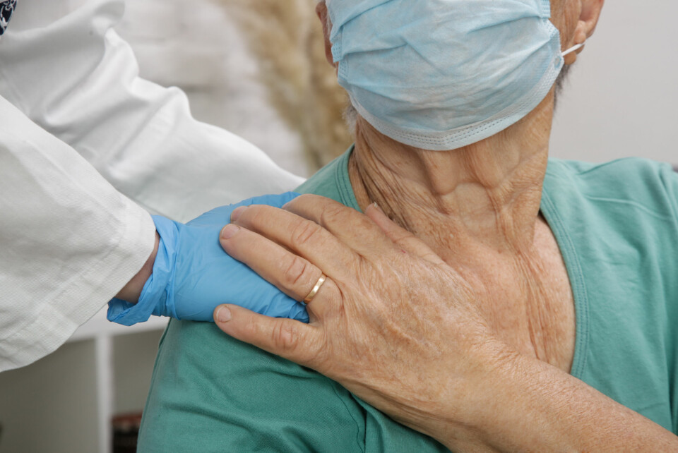 A nurse puts a hand on the shoulder of an elderly woman wearing a mask