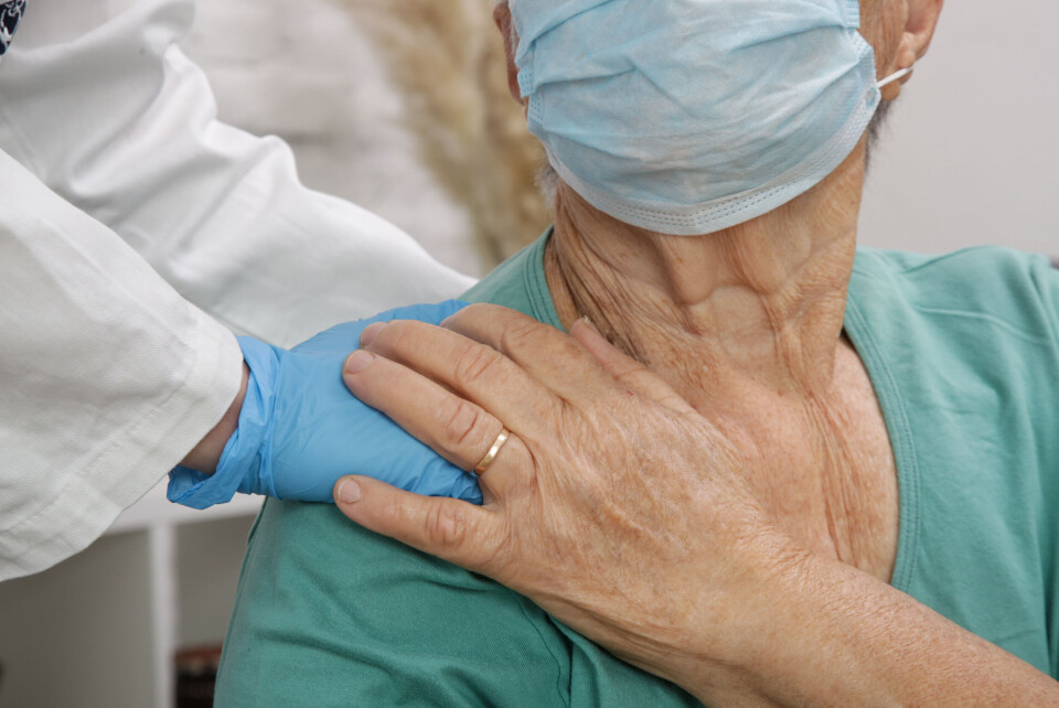 A nurse puts a hand on the shoulder of an elderly woman wearing a mask